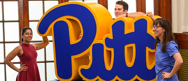 Three grad students pose with Pitt logo art