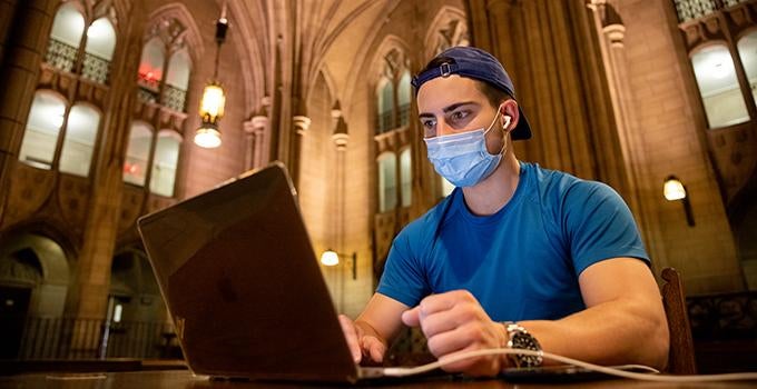 student wearing facemask and using laptop computer