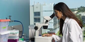 woman in labcoat looking through microscope in laboratory