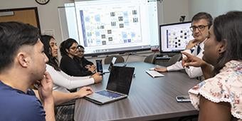 Students and instructor gather around table with lesson on screen at front of room