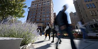 silhouettes of people walking outside past the William Pitt Union; one figure is blurred suggesting fast movement.